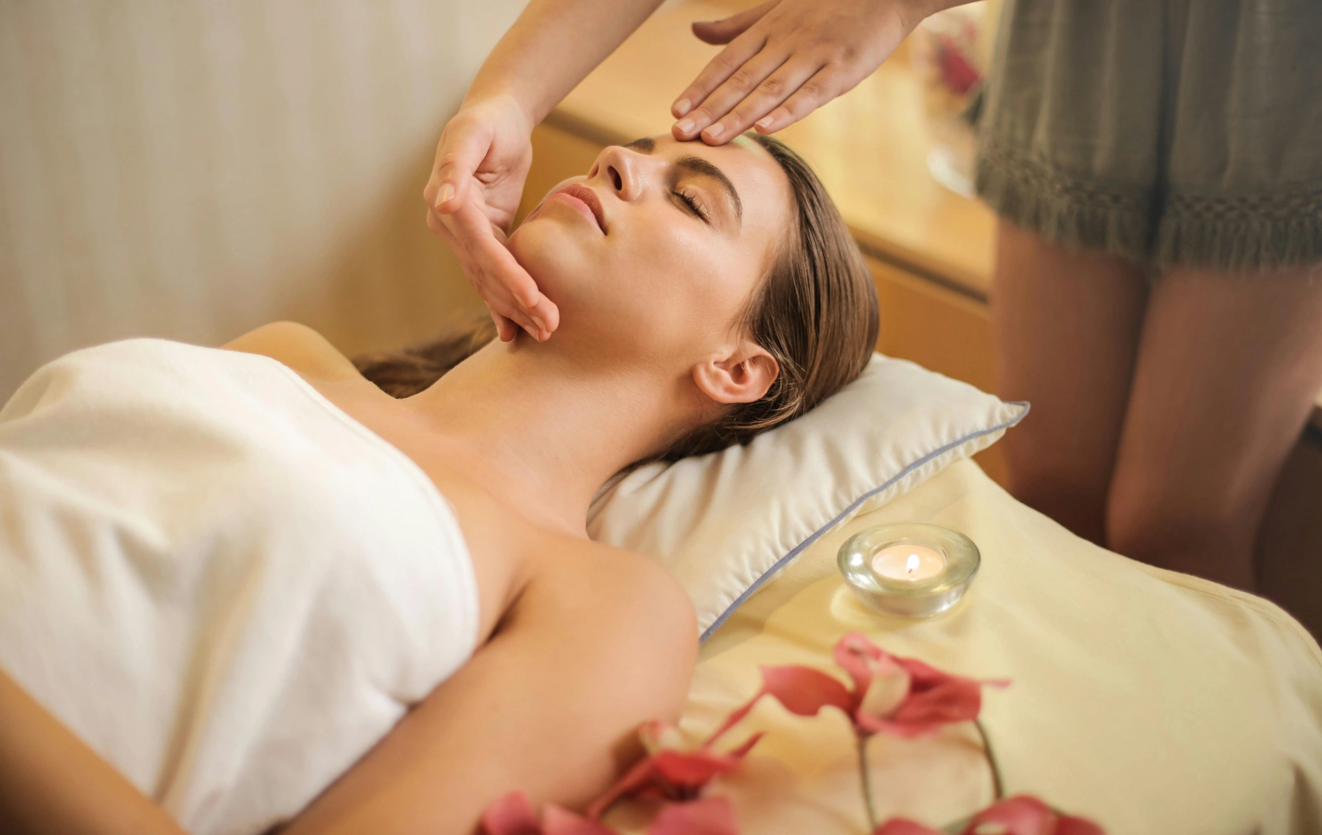 A person relaxing during a facial massage with a candle and flowers nearby.