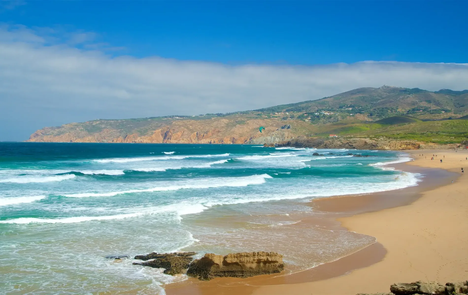 Coastal beach scene with waves, rocky cliffs, and a clear blue sky.