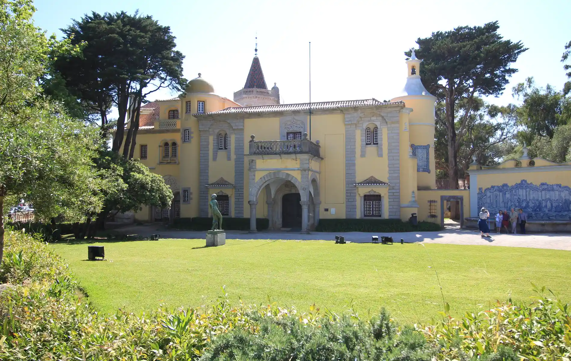 Yellow mansion with arched entrance, surrounded by trees and greenery.