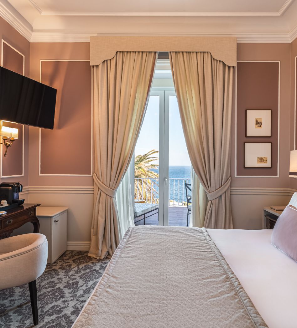 Hotel room with sea view through large window and elegant beige curtains.