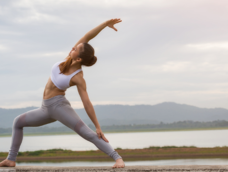 Person doing yoga outdoors near a lake, wearing workout clothes, posing in a side stretch.