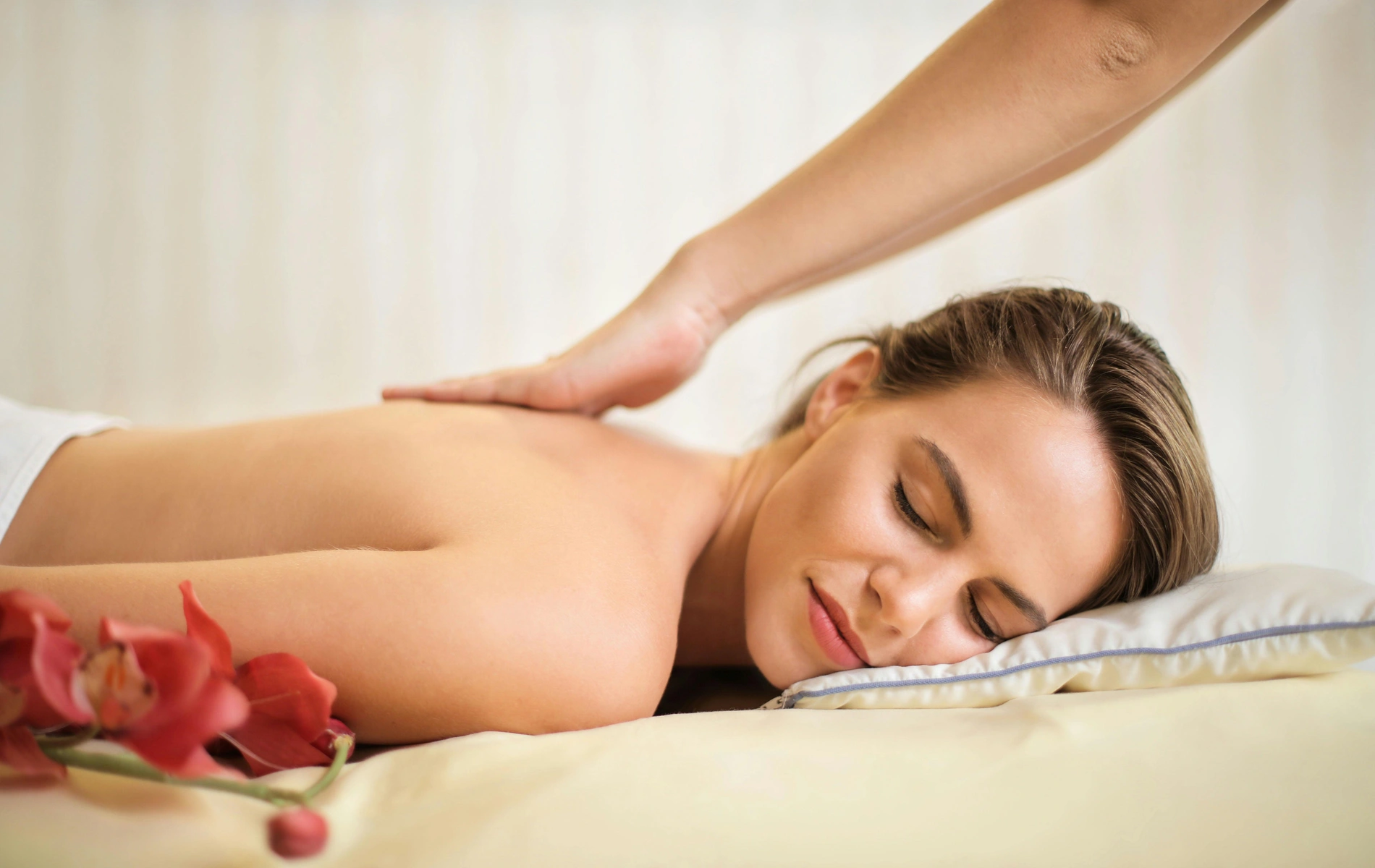 Person enjoying a relaxing back massage while lying on a pillow with flowers nearby.