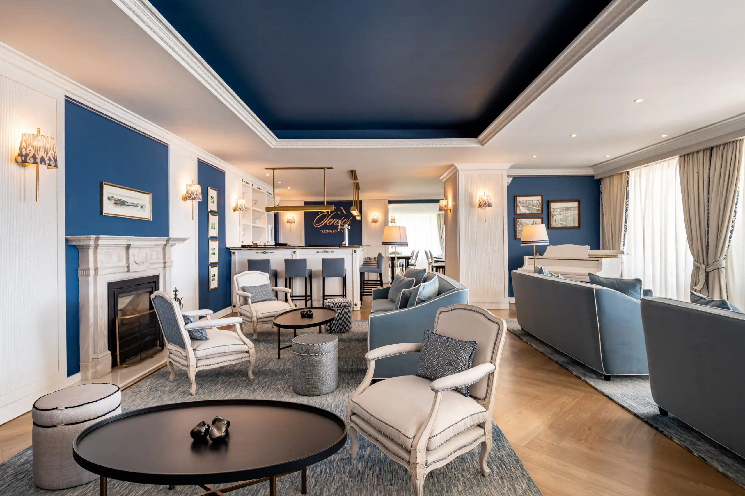 Elegant living room with blue and white decor, sofas, armchairs, and a bar area.