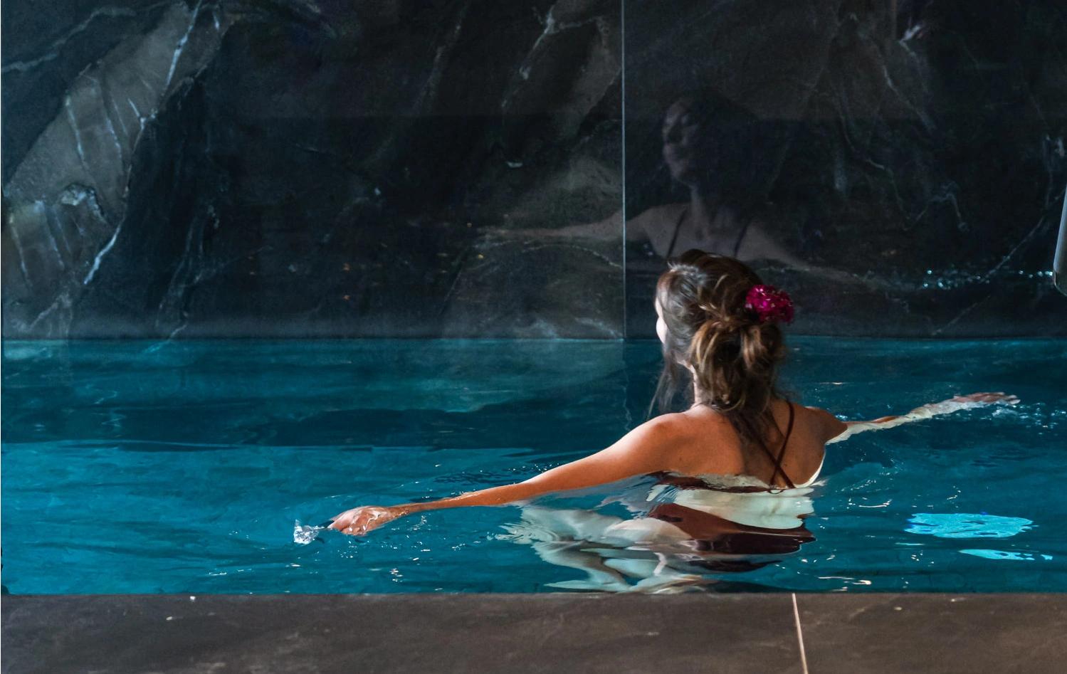 Woman in a pool with her back turned, in a tranquil, dimly-lit setting.