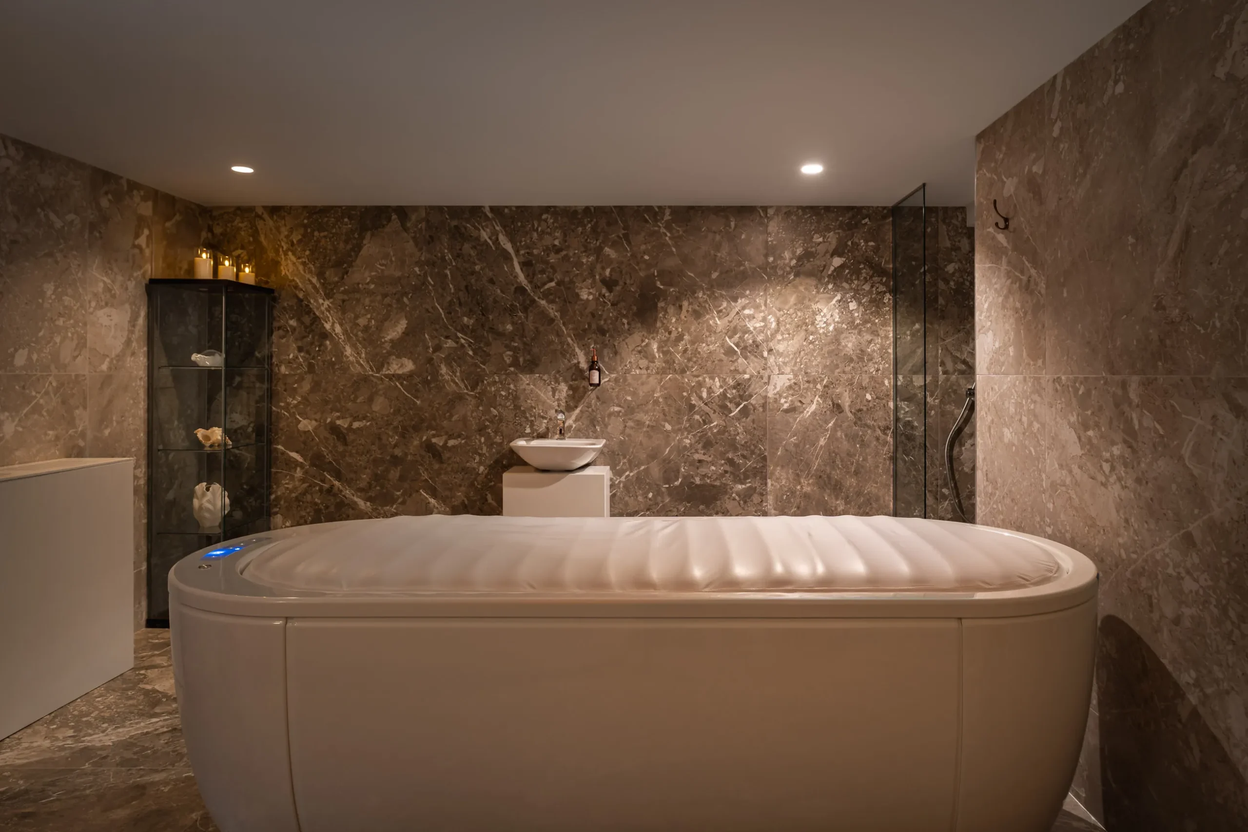 Luxurious marble bathroom with a modern bathtub, glass shelves, and soft lighting.