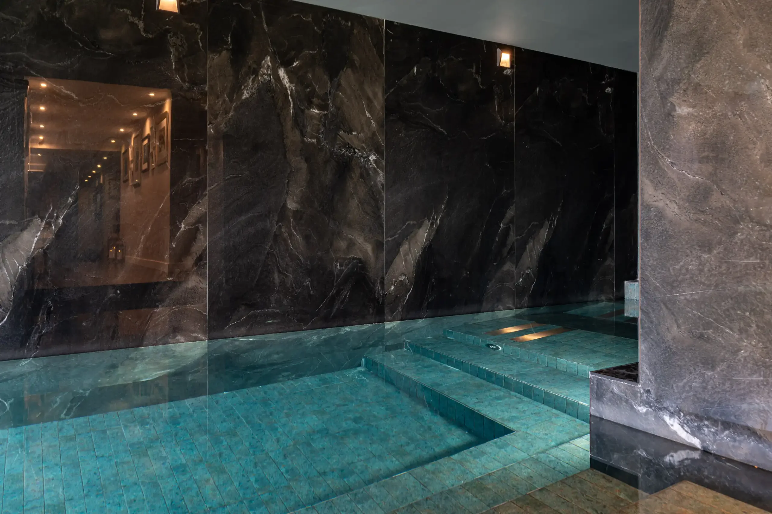 Luxurious indoor pool with dark stone walls and a tile floor.