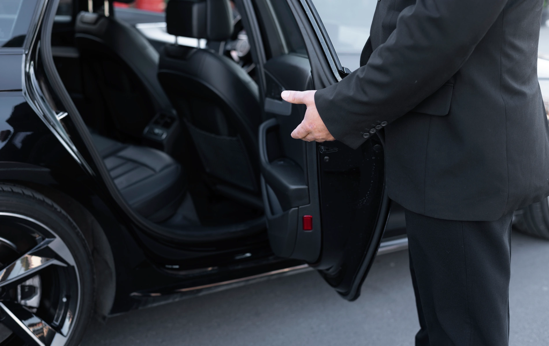 A person in a suit holding open a car door.