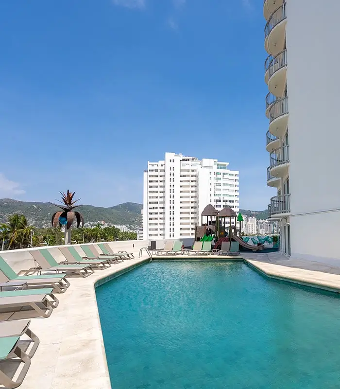 Piscina en una terraza con tumbonas y una vista de edificios y monta&ntilde;as bajo un cielo azul.