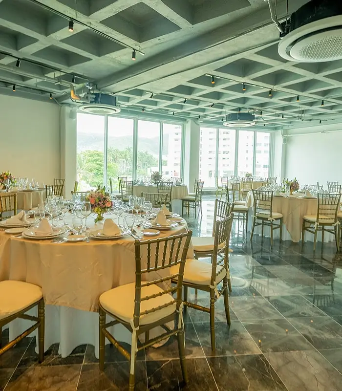 Sala con mesas redondas elegantemente dispuestas, vistas panor&aacute;micas y sillas doradas.