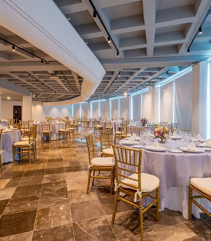 Sal&oacute;n elegante con mesas redondas y sillas doradas, listo para un evento formal.