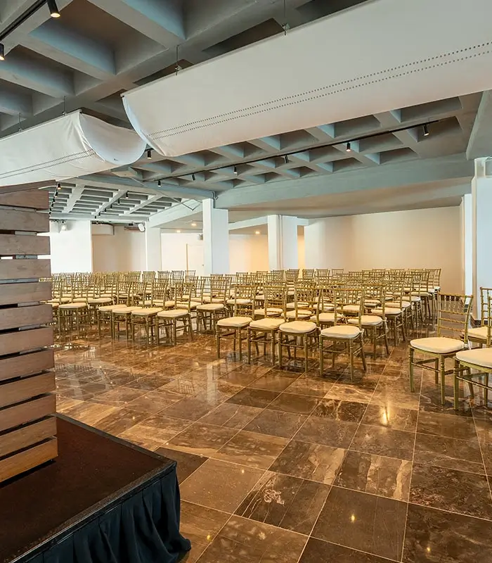 Sala de conferencias con filas de sillas doradas y suelo de m&aacute;rmol.