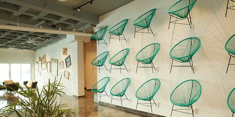 Sillas verdes colgando en una pared en un espacio moderno con cuadros y plantas decorativas.
