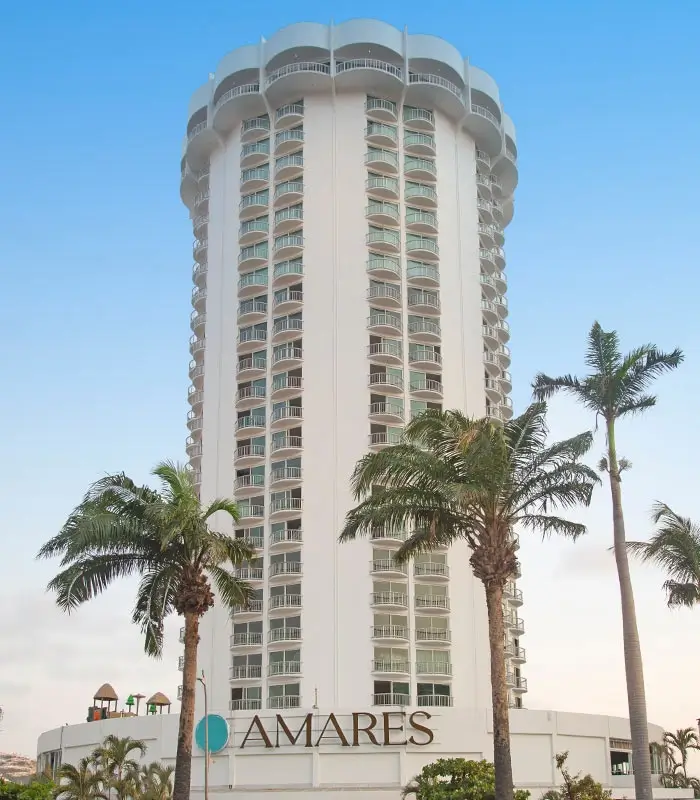 Edificio alto rodeado de palmeras con un letrero que dice "AMARES" al frente.