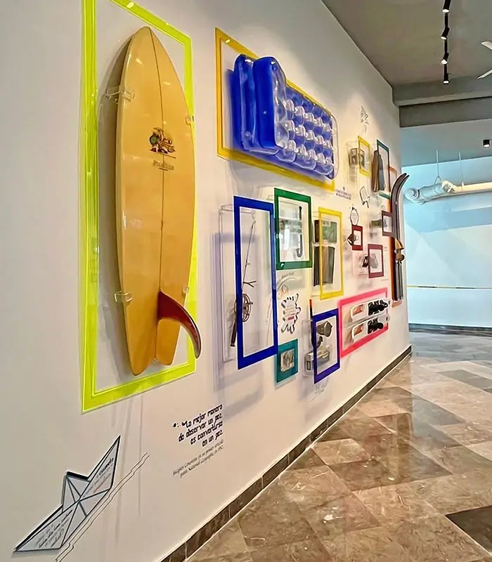 Exhibici&oacute;n de objetos coloridos en una pared, incluyendo una tabla de surf y un colch&oacute;n inflable.