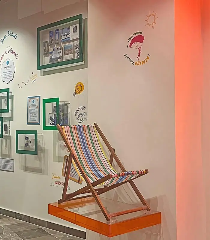 Silla de playa con tela de rayas, en una pared con cuadros y gr&aacute;ficos decorativos coloridos.