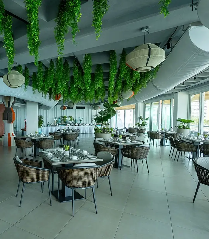 Restaurante con mesas preparadas, plantas colgantes y l&aacute;mparas decorativas en el techo.