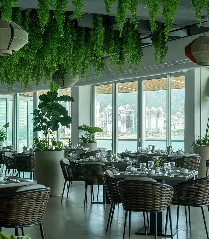 Restaurante elegante con techo decorado de plantas y grandes ventanales con vista a la ciudad.