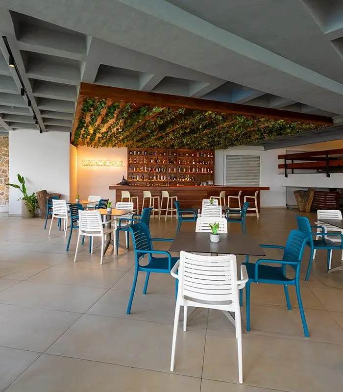 Espacio moderno de restaurante con sillas azules y blancas, barra con botellas y techo con plantas.