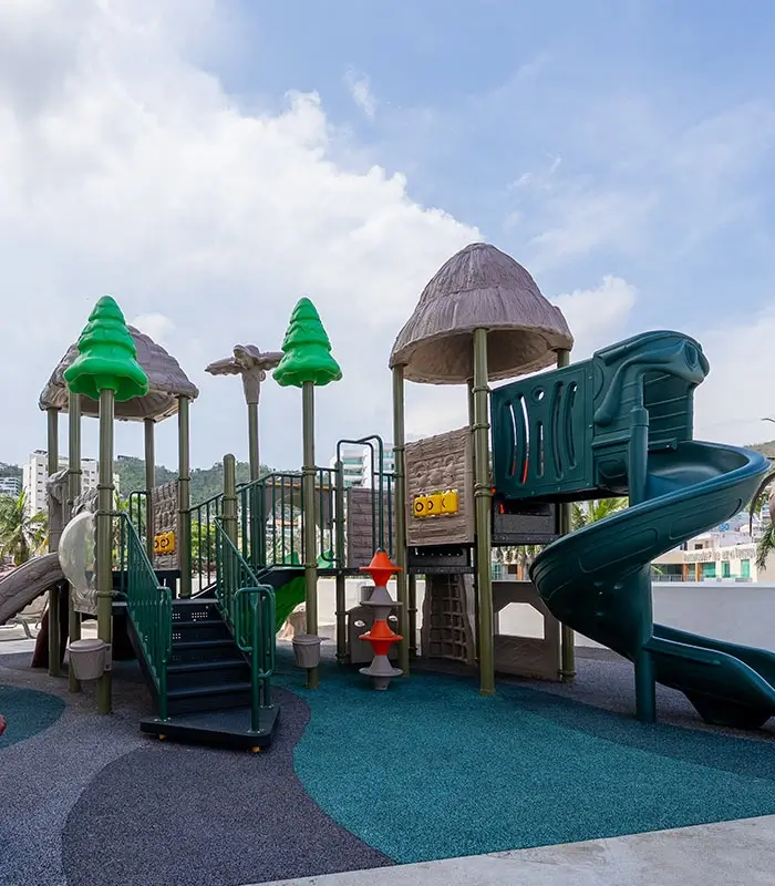Parque infantil al aire libre con tobog&aacute;n y estructuras de juego en forma de &aacute;rbol bajo el cielo azul.