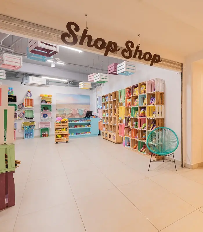 Tienda luminosa con cajas de colores y productos, con letrero "Shop Shop" en la entrada.