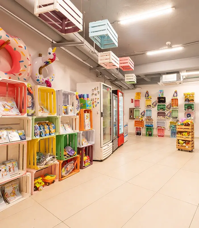 Tienda con estantes de cajas de colores y refrigeradores; flotadores y juguetes para piscina.