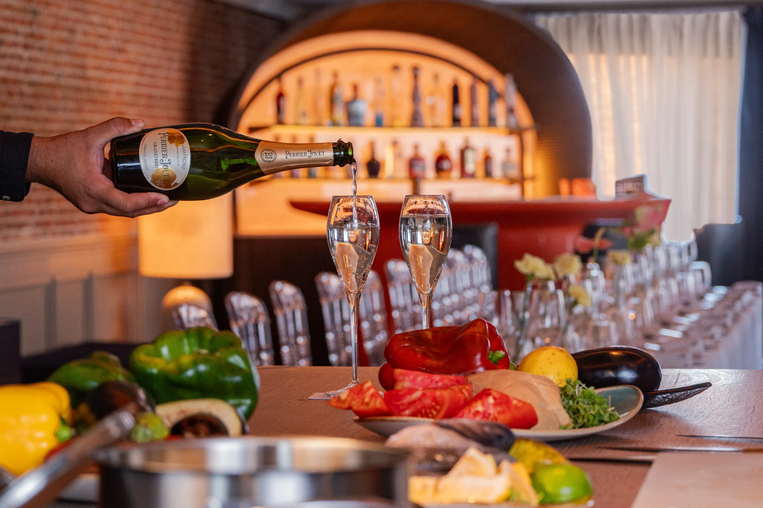 Persona sirviendo champagne en copas con platillo de verduras en un restaurante elegante.