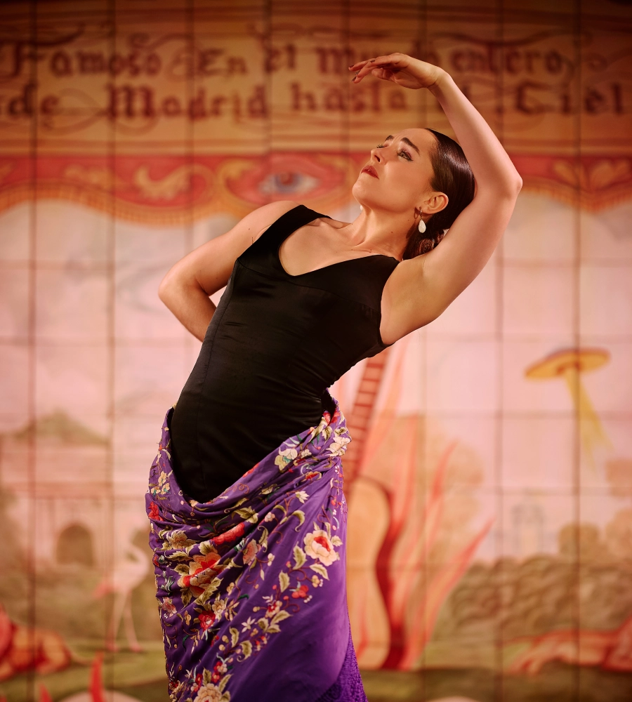 Bailarina de flamenco en pose elegante, con vestido negro y mant&oacute;n p&uacute;rpura, fondo con texto decorativo.