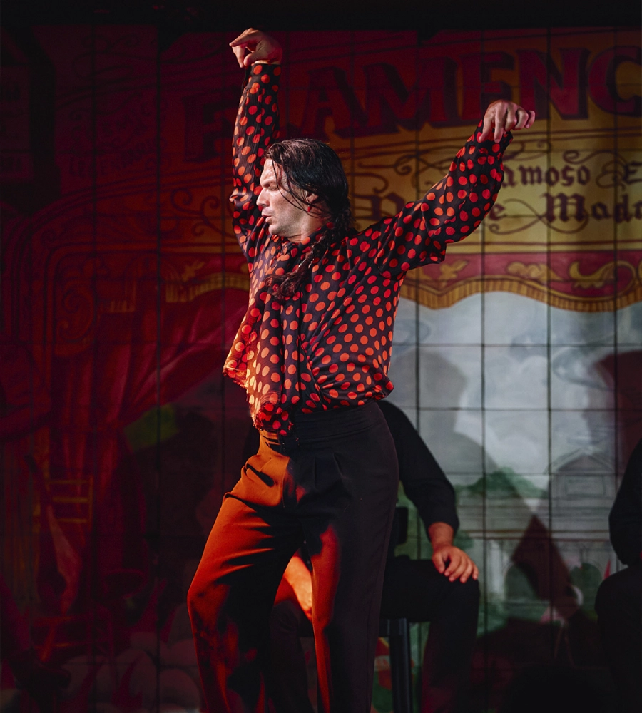 Persona bailando flamenco con una camisa roja de lunares en un escenario con fondo de pancarta.