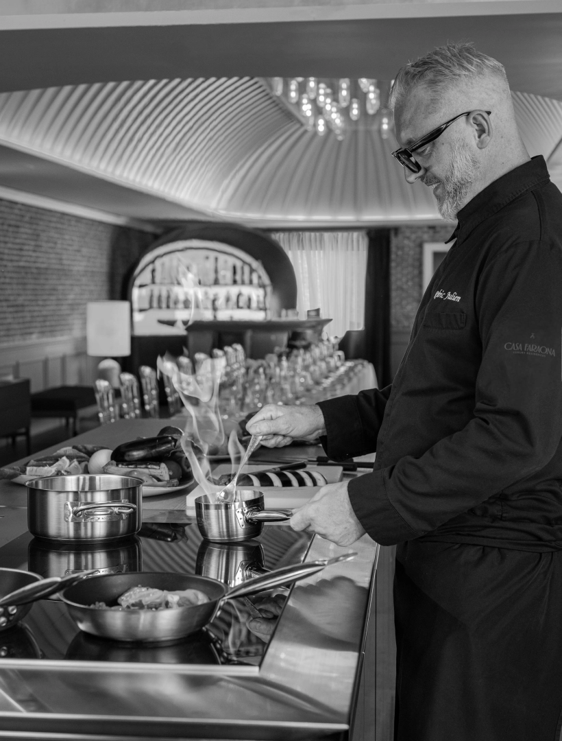 Chef cocinando en una cocina moderna, rodeado de utensilios y alimentos, con vapor saliendo de una olla.
