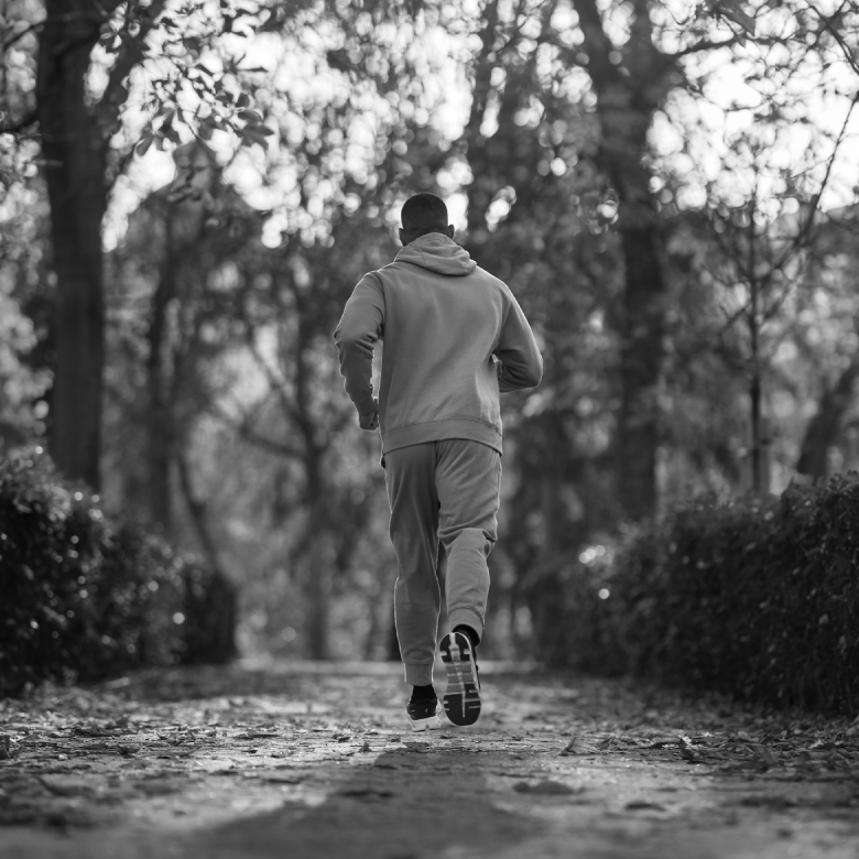 Persona corriendo por un sendero rodeado de &aacute;rboles en un parque. Escena en blanco y negro de un d&iacute;a nublado.