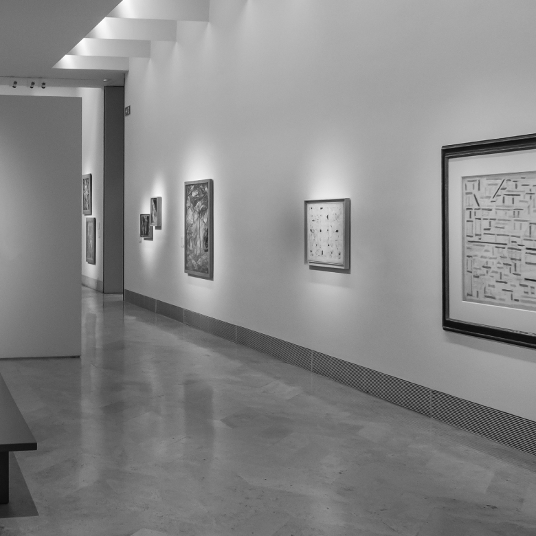 Pasillo de galer&iacute;a de arte con varias pinturas en las paredes iluminadas y suelo de m&aacute;rmol.