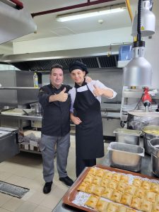 Dos chefs dan un pulgar arriba en una cocina, con pasteles horneados en primer plano.
