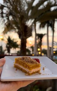Pastel en un plato frente a un atardecer con palmeras de fondo.