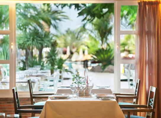 Mesa de restaurante con vista a un jardín tropical a través de grandes ventanas.