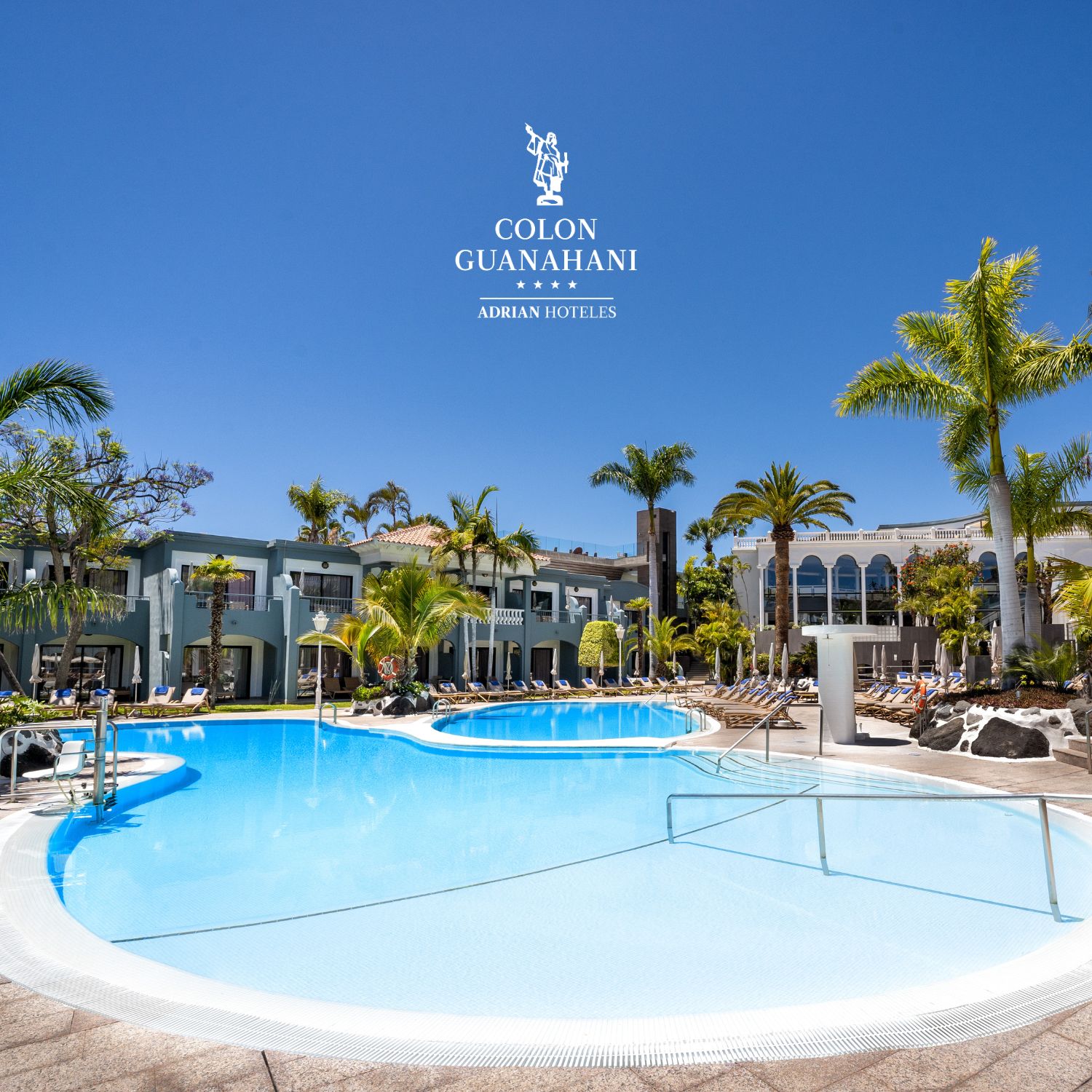 Piscina con palmeras y hotel al fondo bajo un cielo despejado. Texto: "Col&oacute;n Guanahani".