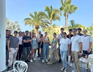Grupo de personas posando al aire libre con palmeras al fondo.