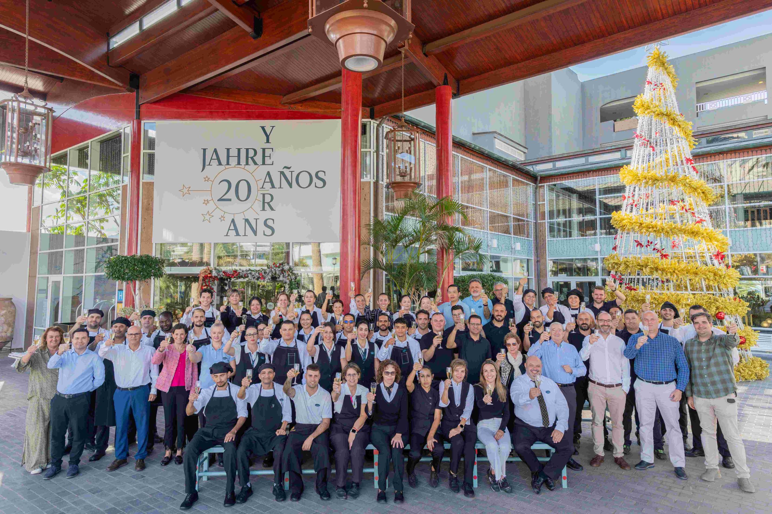 Grupo de personas celebra 20 a&ntilde;os juntos frente a un &aacute;rbol navide&ntilde;o.