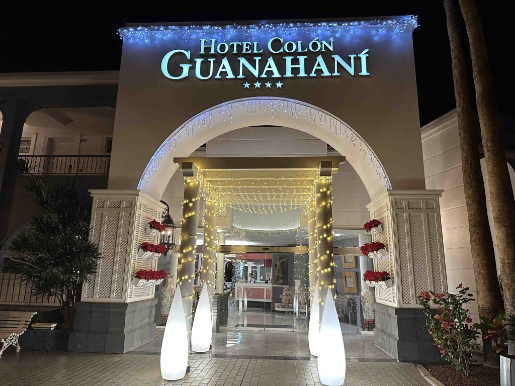 Entrada iluminada del Hotel Col&oacute;n Guanahan&iacute; con decoraciones festivas y plantas.