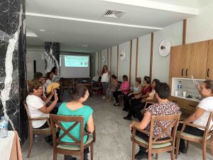 Personas en un taller sentadas en c&iacute;rculo, escuchando a una instructora en una sala con proyecci&oacute;n.