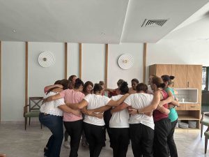 Un grupo de personas se abraza en c&iacute;rculo en una sala luminosa y moderna.