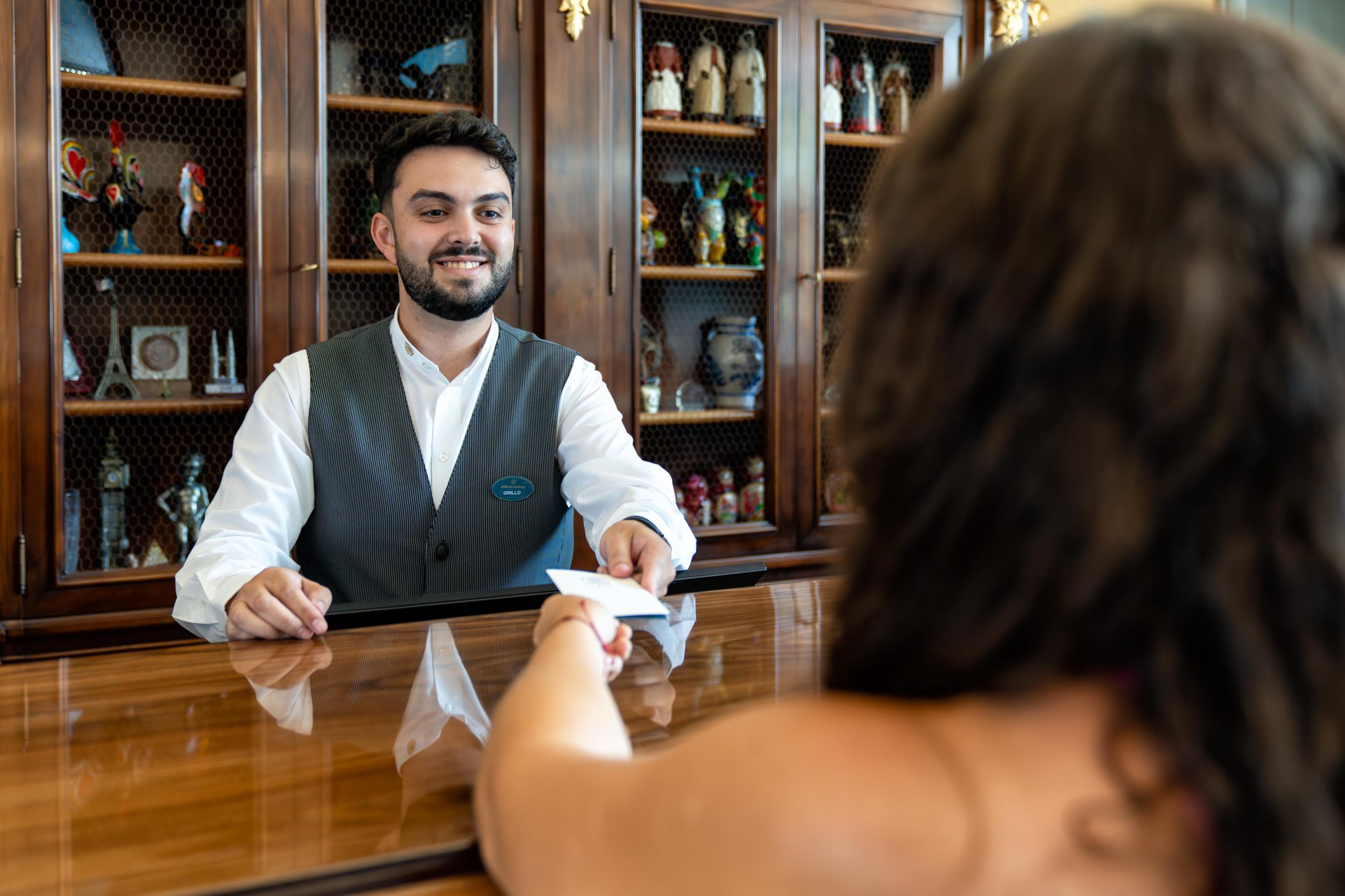 Persona sonriente entregando una tarjeta a un cliente en la recepci&oacute;n de un hotel.