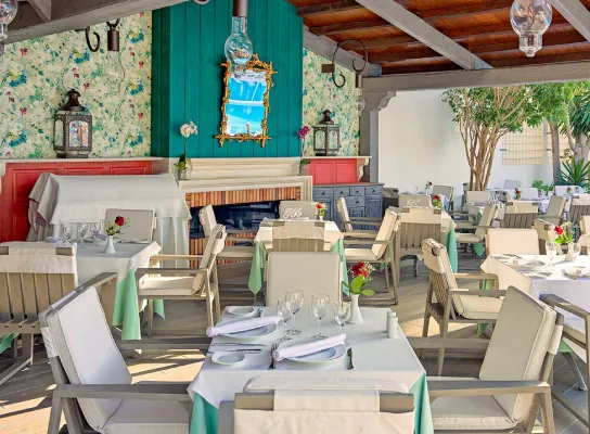 Restaurante al aire libre con mesas preparadas, muebles de madera y decoración colorida.