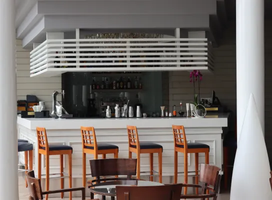 Bar con sillas altas de madera, botellas al fondo y mesa redonda en primer plano.