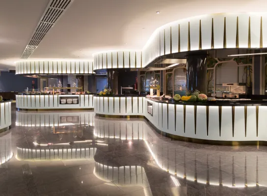 Buffet moderno con iluminación elegante y decoración de frutas sobre mostradores curvos blancos.