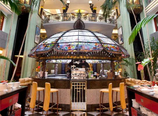 Bar estilo art nouveau bajo una cúpula de vidrio colorido, decorado con plantas y luces.