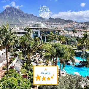 Vista del hotel con piscina, jardines tropicales y monta&ntilde;as al fondo. Calificaci&oacute;n: hotel destacado.