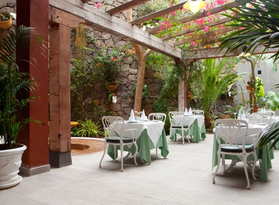Patio de restaurante con mesas decoradas, rodeado de plantas y paredes de piedra.