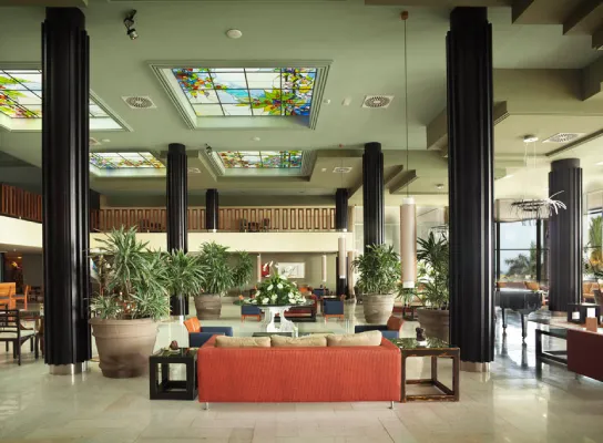 Lobby elegante con columnas negras, vitrales en el techo y muebles en tonos tierra.