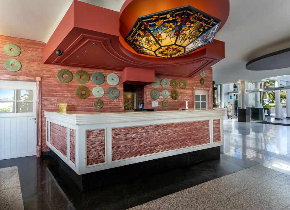 Mostrador de recepción con madera rústica, techo decorado y discos metálicos en la pared.