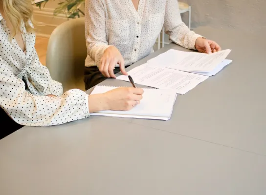 Dos personas revisando documentos en una mesa, señalando con bolígrafos.